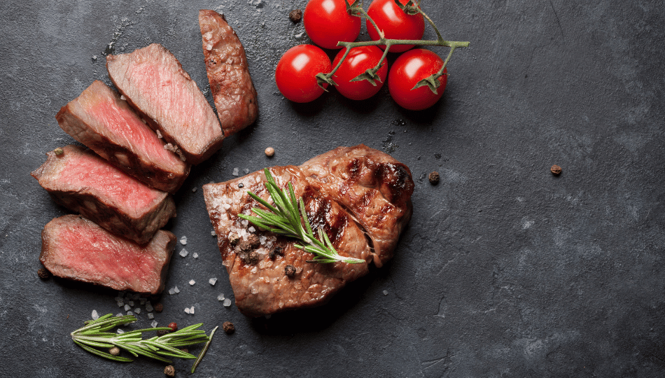 Saftig rosa gebratenes Rumpsteak in Scheiben geschnitten mit Rosmarin, Meersalz und Tomaten auf dunklem Stein – perfekt zubereitet nach dem Rindfleisch Marinieren.